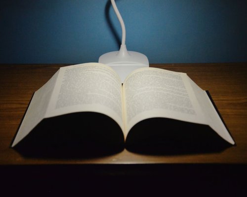 A clean white desk with a small reading lamp illuminating an open hardcover book under gentle shadows
