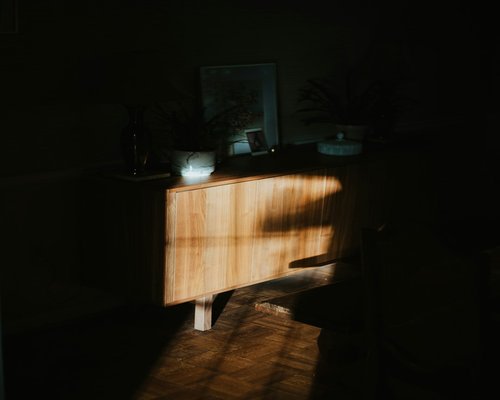 A relaxed evening room setting showing a small soft glowing light source highlighting a wooden side table
